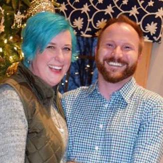 Michelle with blue hair happily standing next to her husband smiling wearing a button up shirt