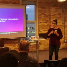 Ellen speaking in front of a slide that asks, "What does inaccessibility feel like?"