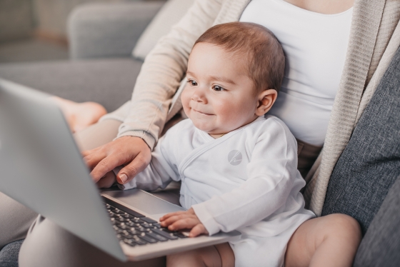 smiling baby in mother's lap typing on laptop