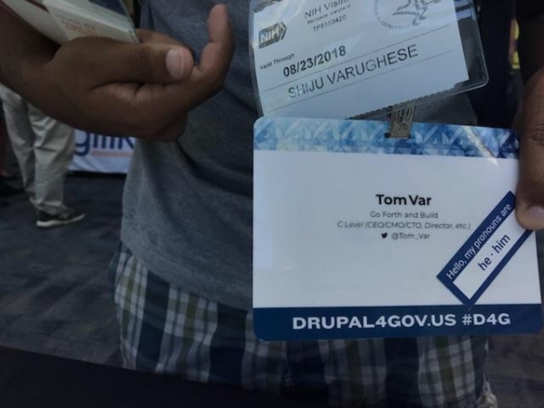 An attendee at DrupalGovCon displaying personal pronoun sticker on their badge